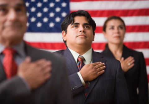 Businesspeople standing in front of an American flag with one hand across their hearts